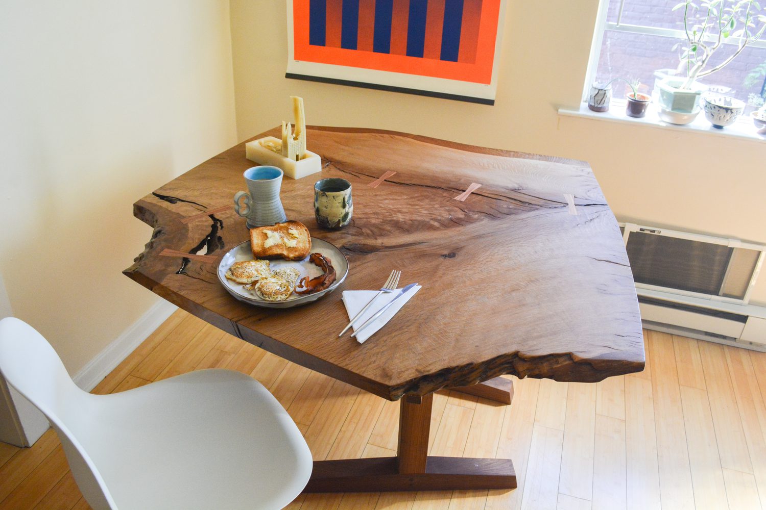 A live-edge walnut dining table set for breakfast in warm morning light, its trestle base wedged together by hand